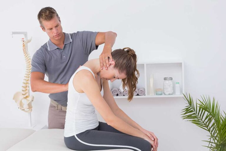 Person gently holding a shoulder while demonstrating arm movement in a bright home setting.