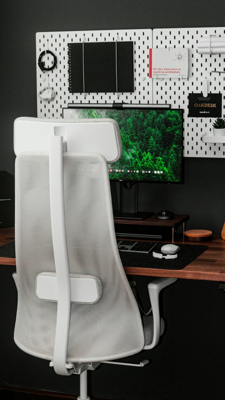 Office worker seated at an organized desk with a raised monitor, supported back, relaxed shoulders, and hands on a keyboard.