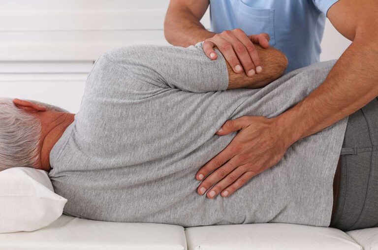 Person gently stretching a sore knee near a window during a cold, snowy day.